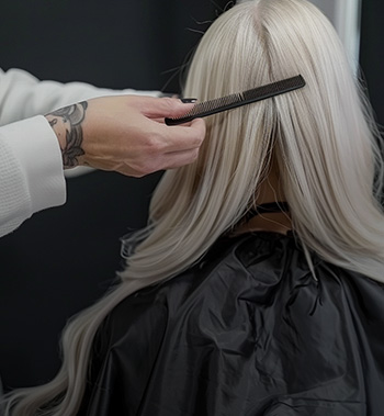 Friseur kämmt sanft langes platinblondes Haar von hinten, Vorbereitung für das Styling oder die Haarverlängerung